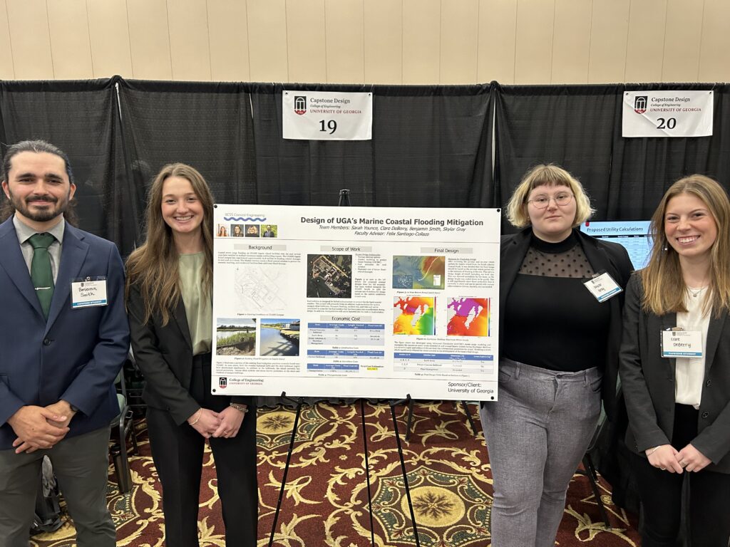 Four university students in business formal attire standing in a conference center around a poster titled "Design of UGA's Marine Coastal Flooding Mitigation", complete with images, tables, text, and graphs